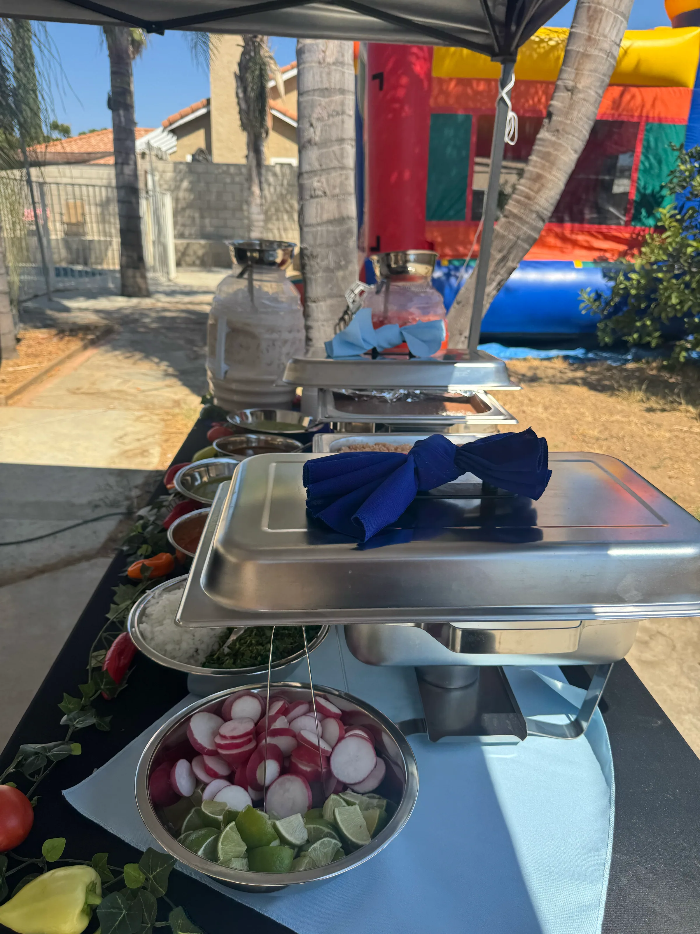 Tacos V buffet at a birthday party with taco toppings, chafing dishes, and a bounce house in the background