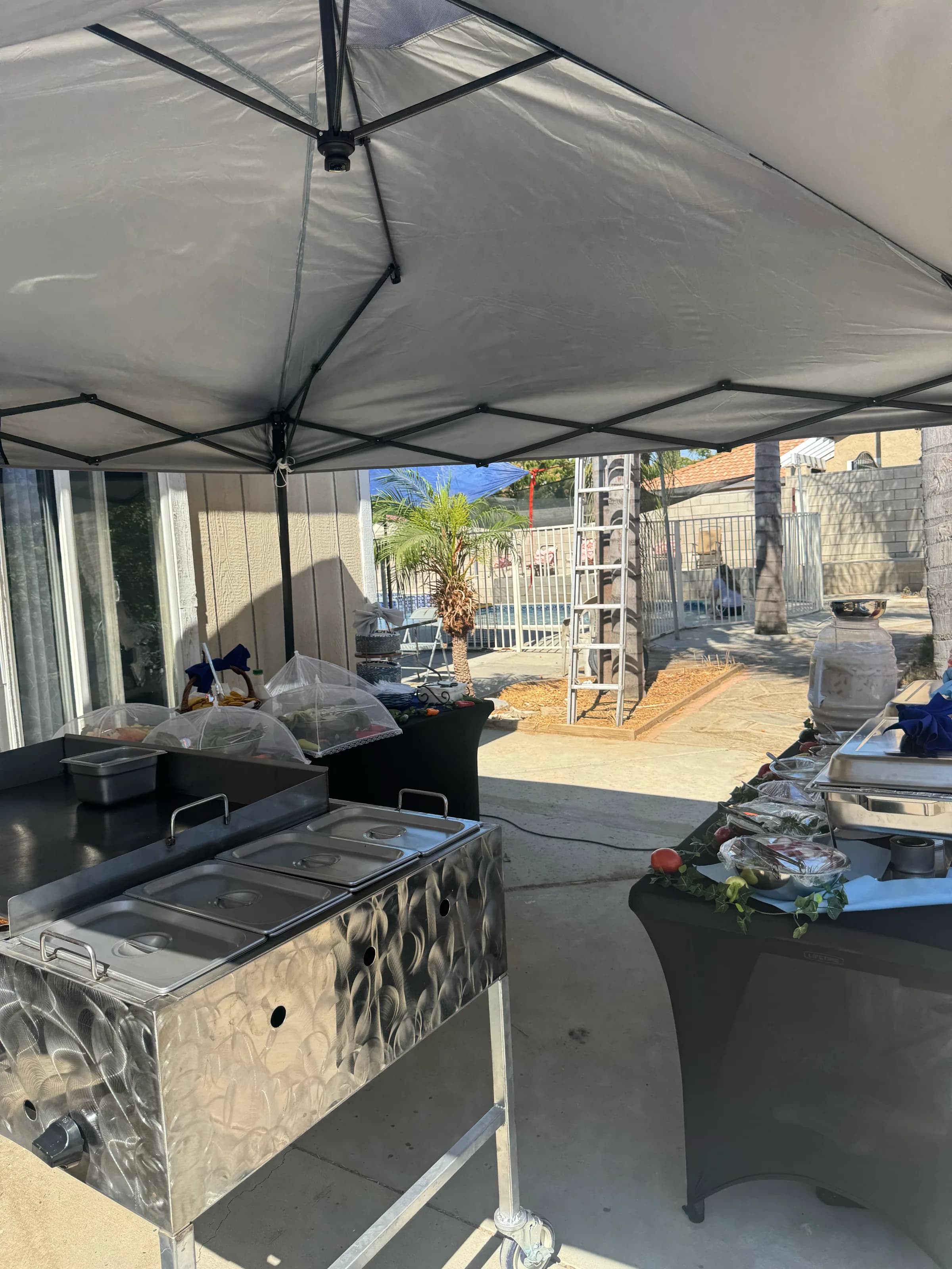 Tacos V griddle station and full buffet under a white canopy at a poolside catering event