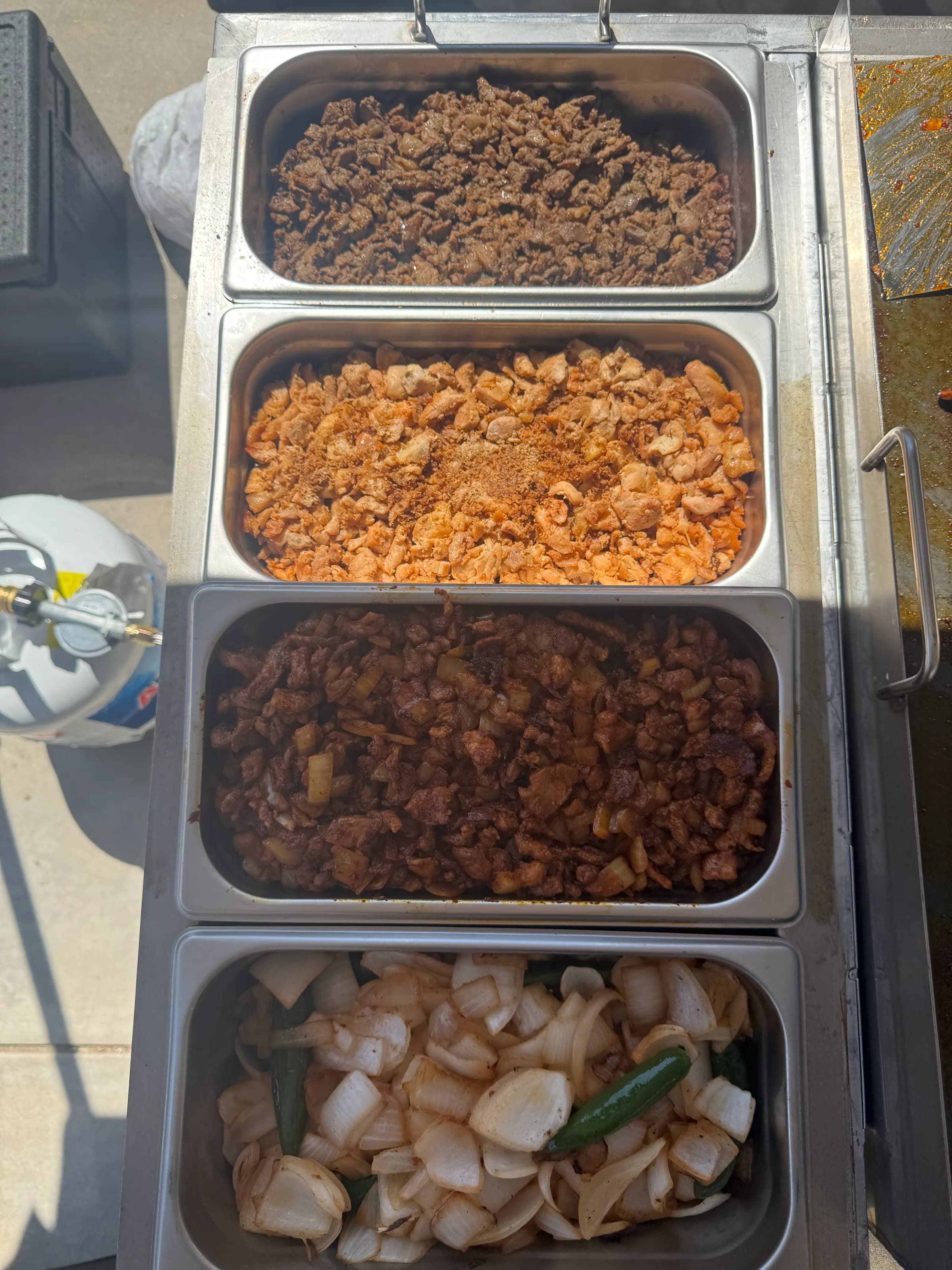 Four hotel pans showing Tacos V's taco meats, carne asada, al pastor, and grilled onions with jalapeños