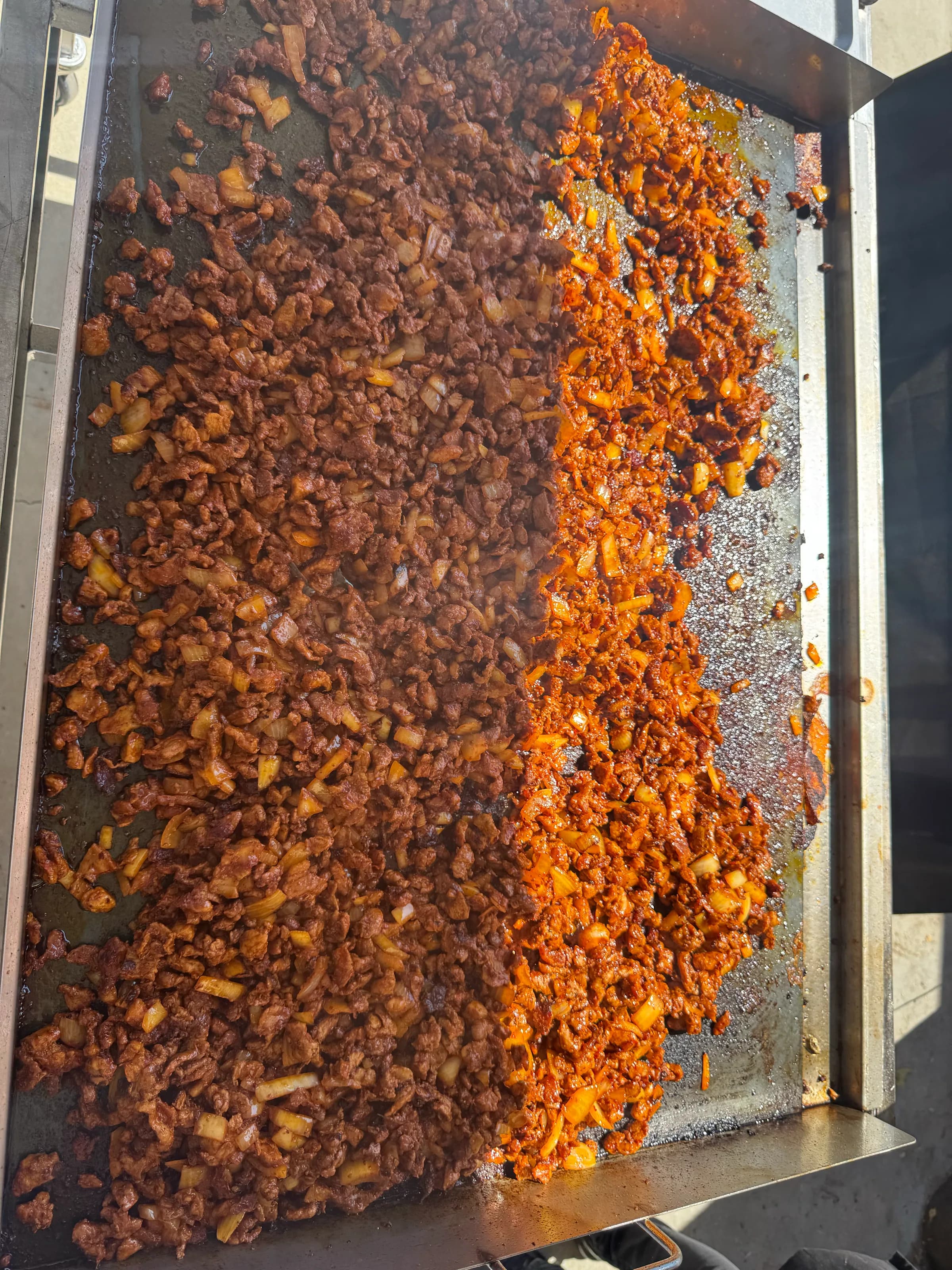 Carne asada and al pastor sizzling side by side on a Tacos V flat-top grill at a catering event