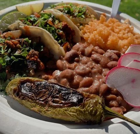Plate of street tacos with carne asada and al pastor, served with Mexican rice, refried beans, a grilled jalapeño, and radish garnish